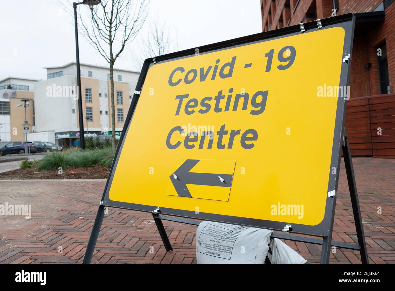 Cartello stradale giallo in piedi libero per la lettura Covid-19 Testing Center con il simbolo della freccia direzionale che indica la strada. Foto Stock