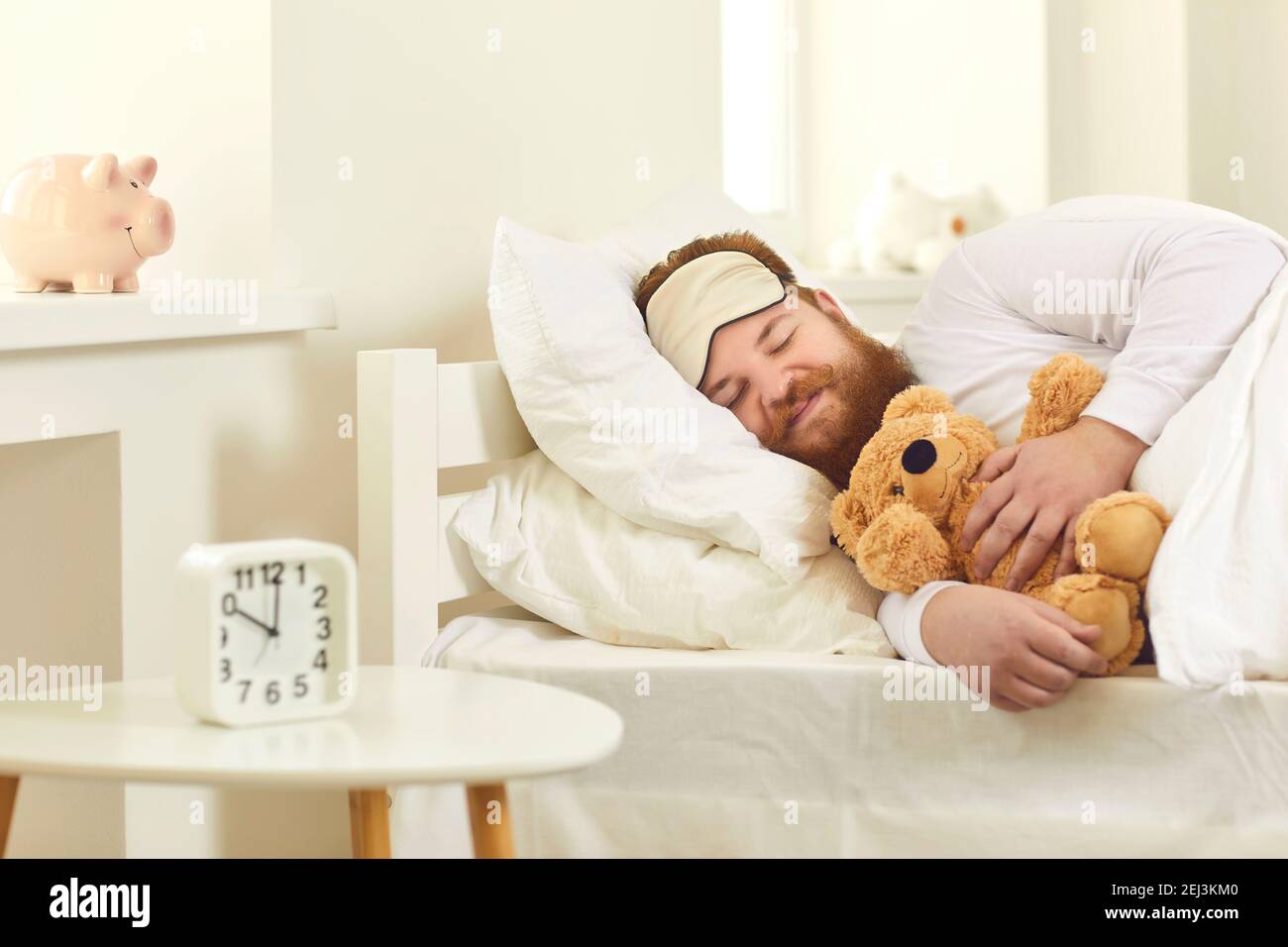 Uomo adulto sdraiato in un comodo letto, coccolante orsacchiotto e sognare dolci sogni Foto Stock