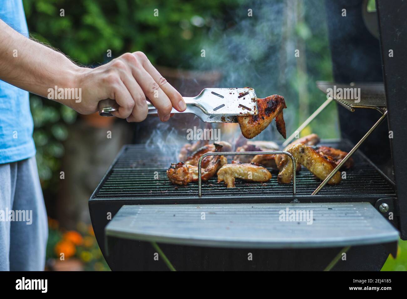 Barbecue pollo ala sulla griglia durante la festa in giardino. Uomo con forchetta grigliando carne marinata in estate all'aperto Foto Stock