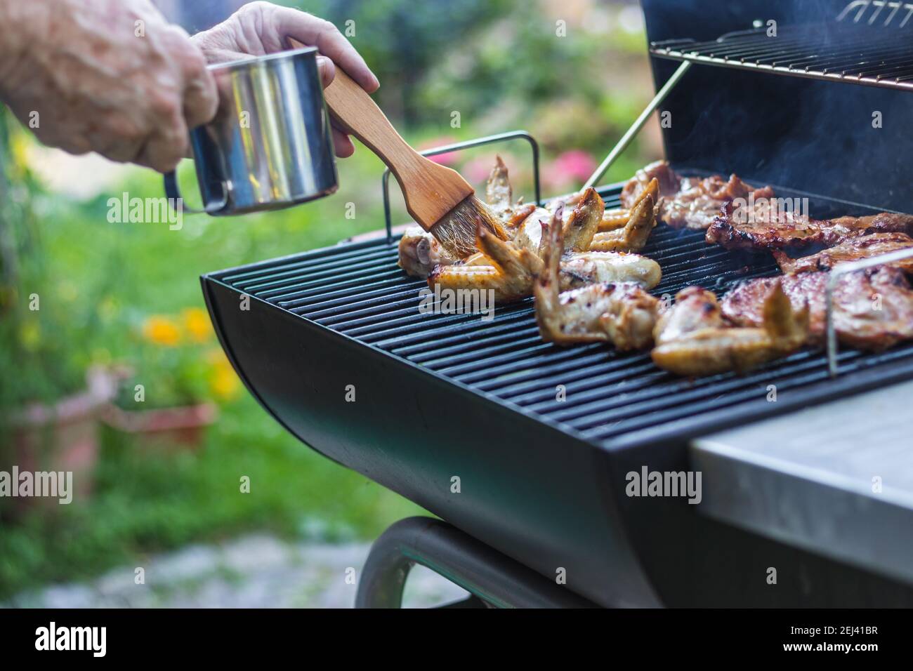 Mano con pennello per la cottura marinare la carne sulla griglia durante la  festa in giardino. Barbecue estivo all'aperto Foto stock - Alamy