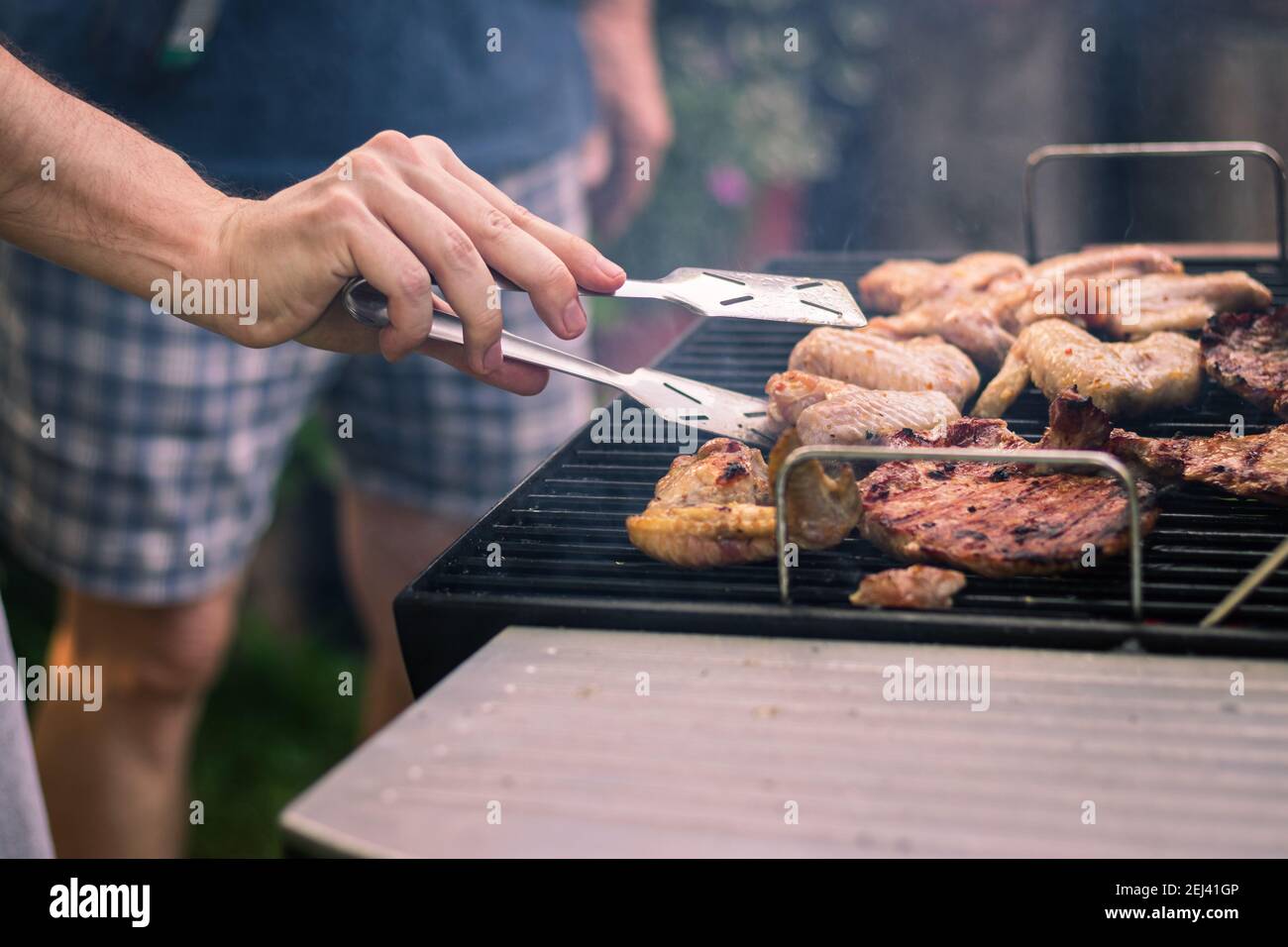 Barbecue di carne alla griglia durante la festa in giardino. Persone che cucinano pollo marinato e bistecca al barbecue estivo all'aperto. Foto Stock