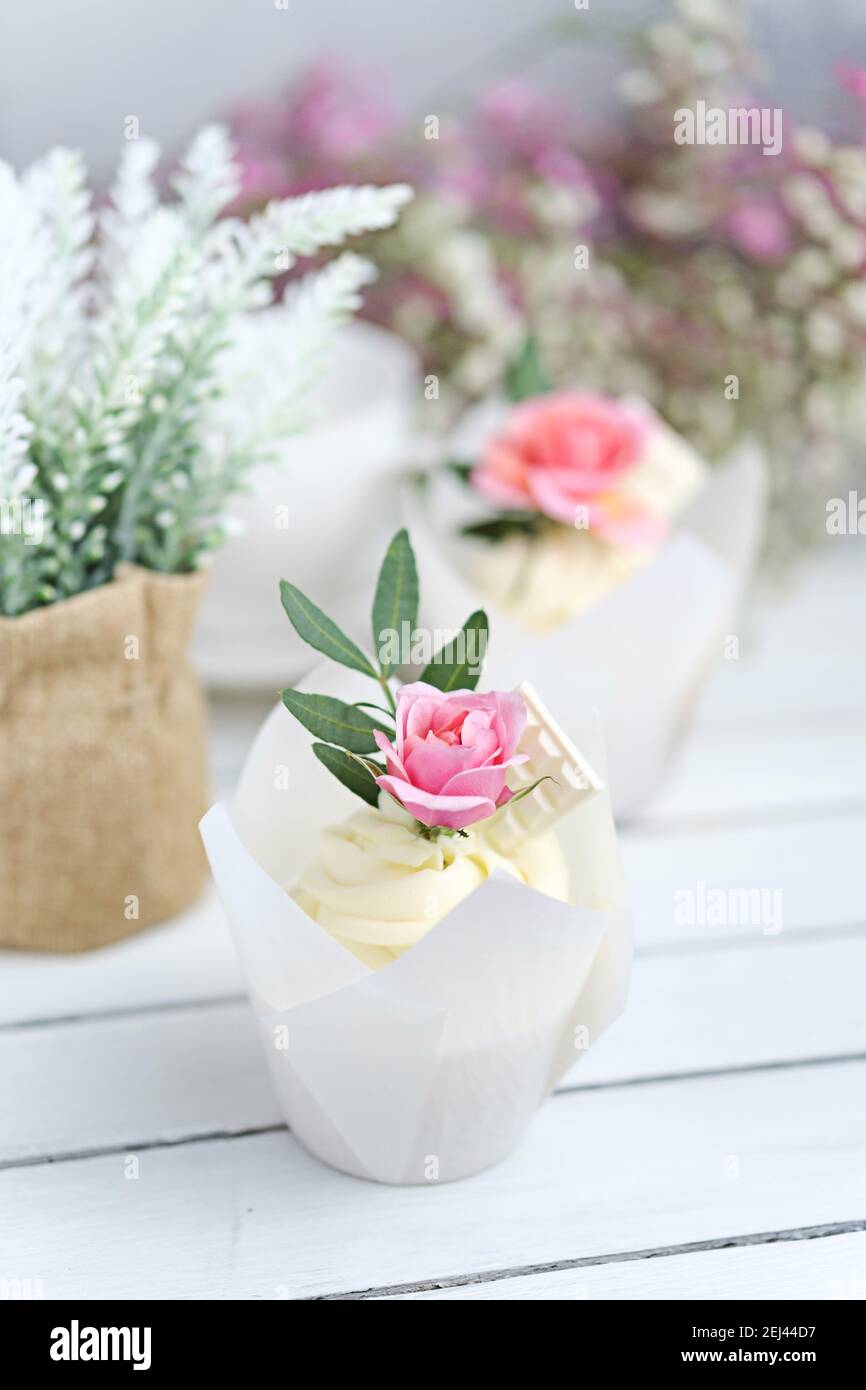 Numerosi cupcake e muffin con panna bianca al burro e una vivace rosa su un tavolo di legno bianco. San Valentino o regalo per la festa della mamma. Flusso fresco Foto Stock
