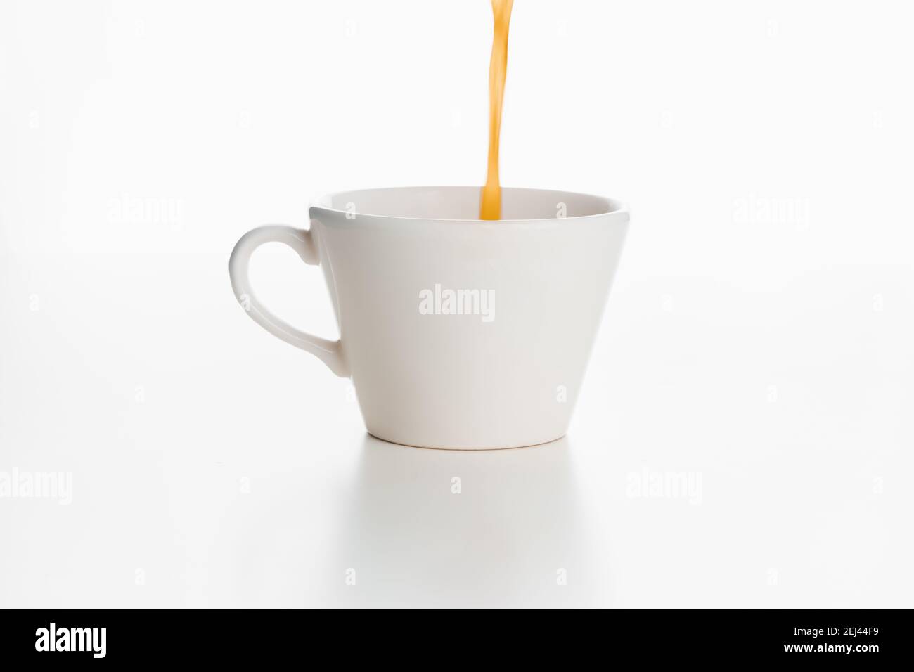 Il caffè viene versato dall'alto in una tazza bianca isolata su una superficie bianca e su uno sfondo. Foto Stock