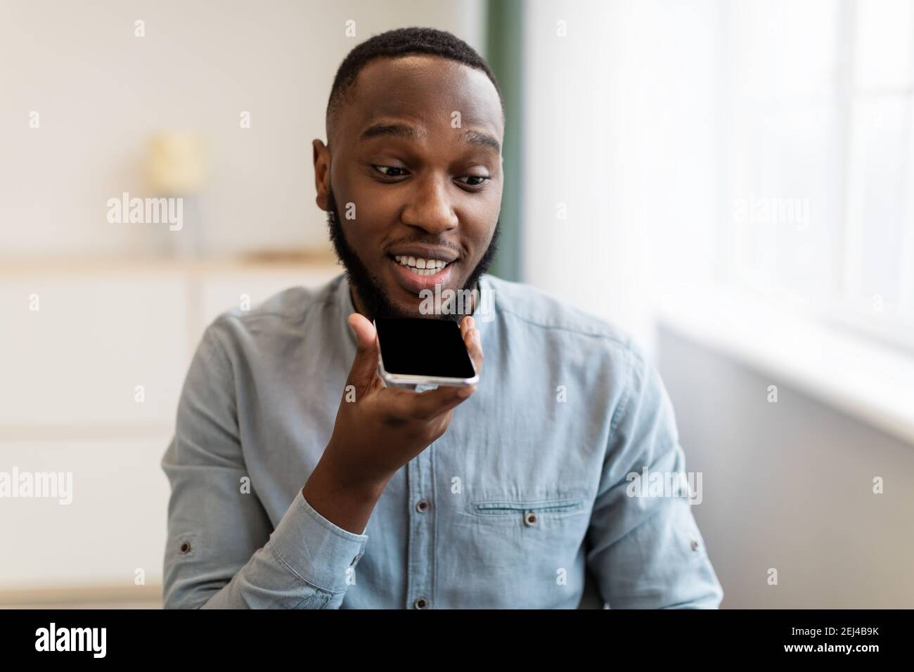Black Guy che usa il telefono cellulare con l'applicazione Assistente vocale sul luogo di lavoro Foto Stock