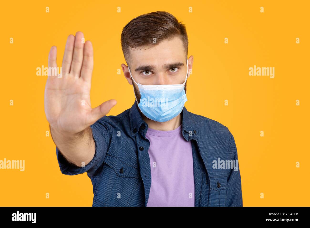 No al coronavirus. Giovane uomo caucasico in maschera medica facendo GESTO DI STOP su sfondo arancione studio Foto Stock
