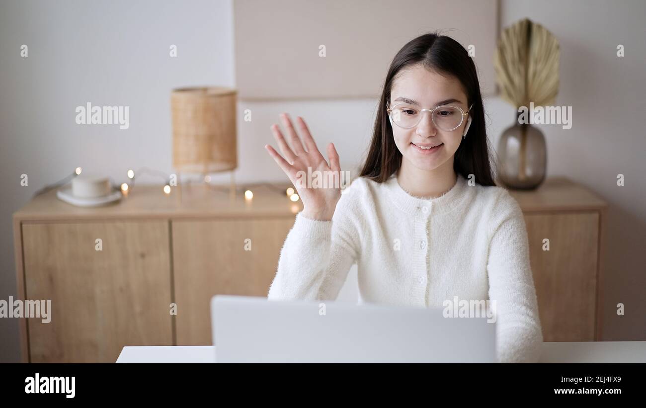 Ragazza adolescente carina che agita la mano con insegnante online sullo schermo del computer portatile a casa. Concetto di istruzione, apprendimento a distanza, autoformazione, cla per videoconferenze Foto Stock