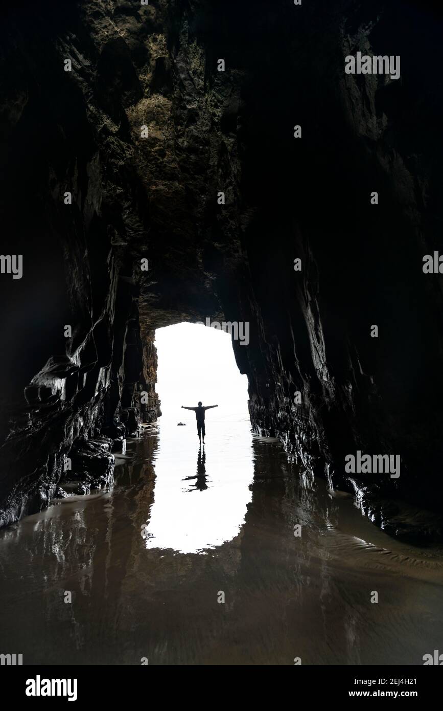 Silhouette di una persona davanti all'uscita della grotta in controluce, grotta bagnata dal mare, Cathedral Cave, Waipati Beach, The Catlins, Southland, Sud Foto Stock