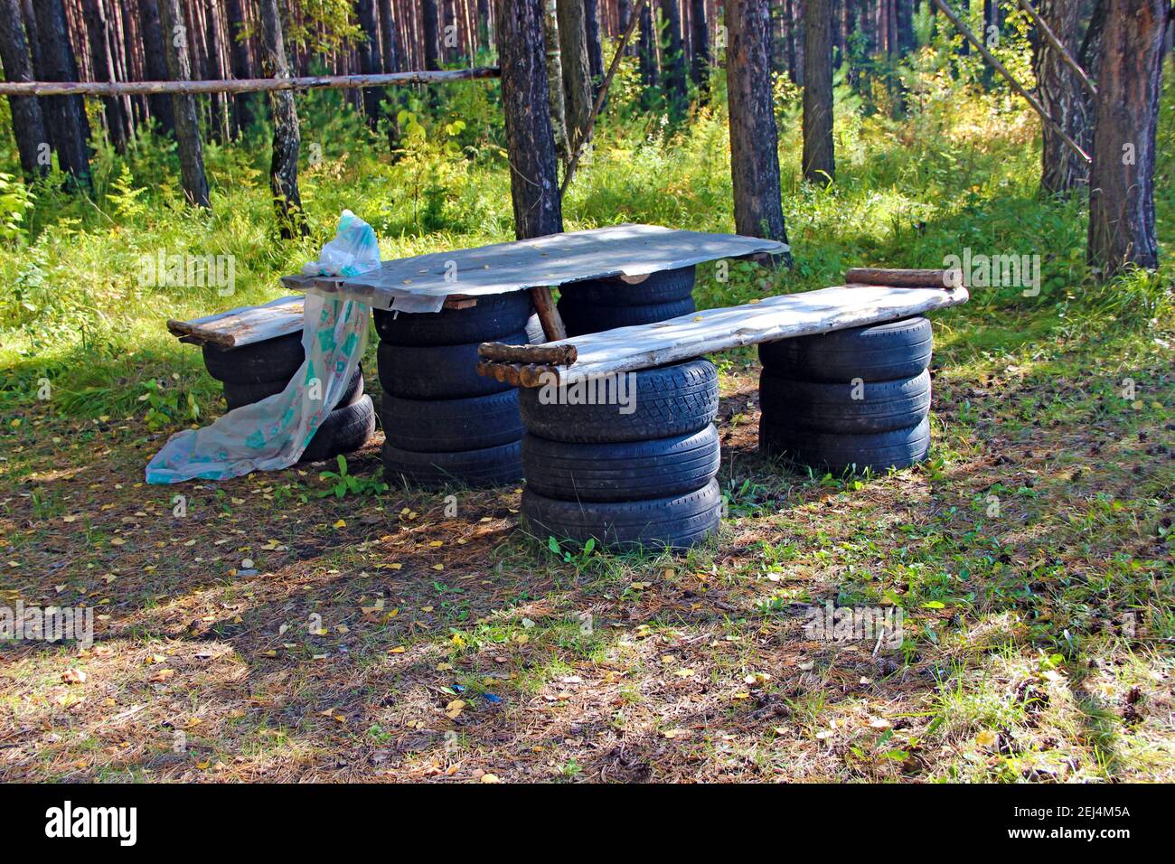 Un posto per riposare nella foresta - un tavolo e panche fatto di vecchie ruote, assi e tronchi di auto. Foto Stock