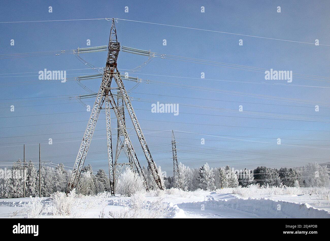 Un'incredibile combinazione della struttura in acciaio del traliccio della linea elettrica con fili tesi in primo piano e la foresta invernale all'orizzonte. Foto Stock