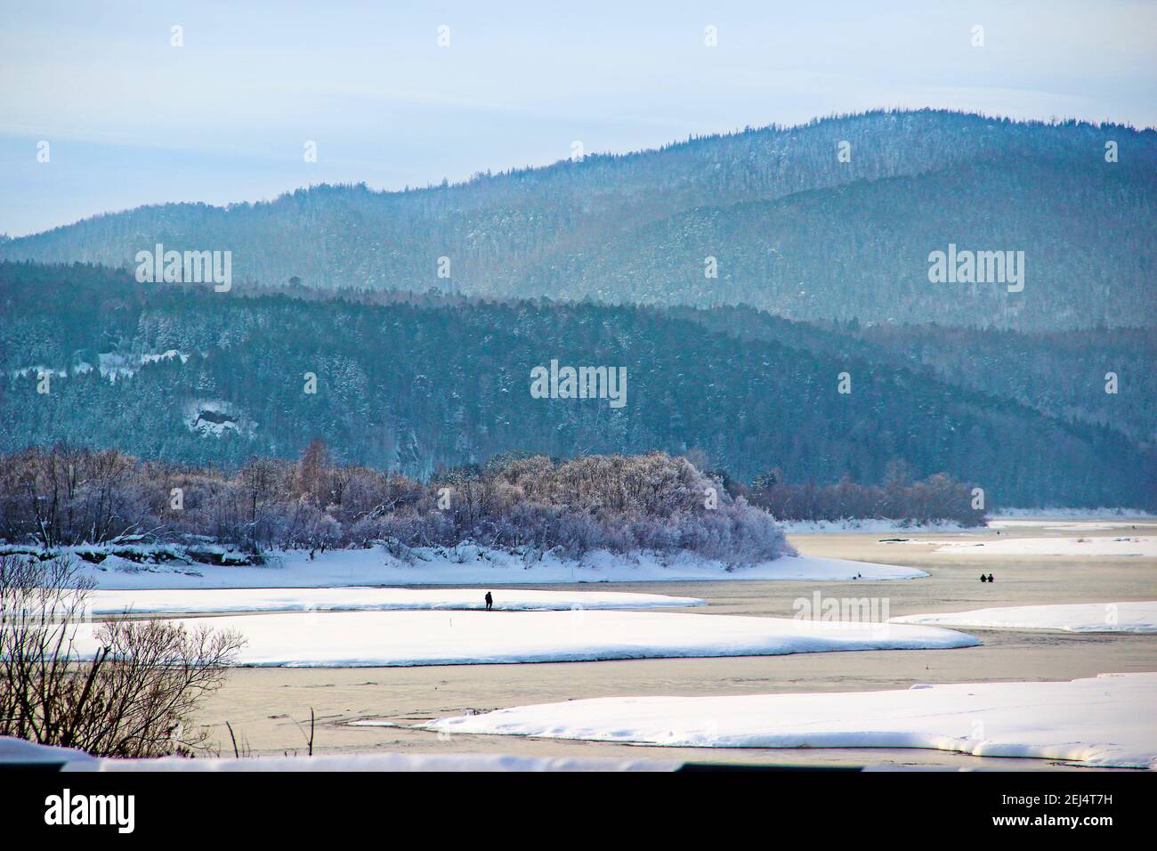 Paesaggio invernale - il fiume corre tra le rive innevate e colline boscose e pescatori sono la pesca. Foto Stock