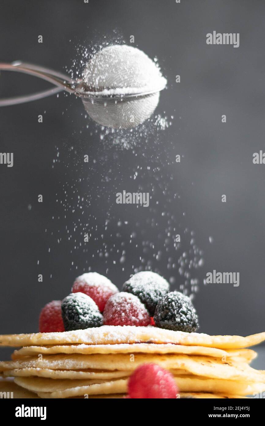 Versare lo zucchero sulle crepes fatte in casa sul tavolo, fotografia di cibo scuro Foto Stock