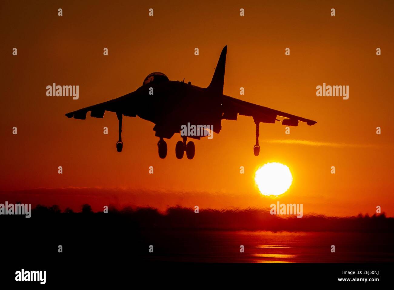 La silhouette del bombardiere da combattimento Harrier atterra al tramonto contro un cielo arancione e un grande sole che tramonta Foto Stock