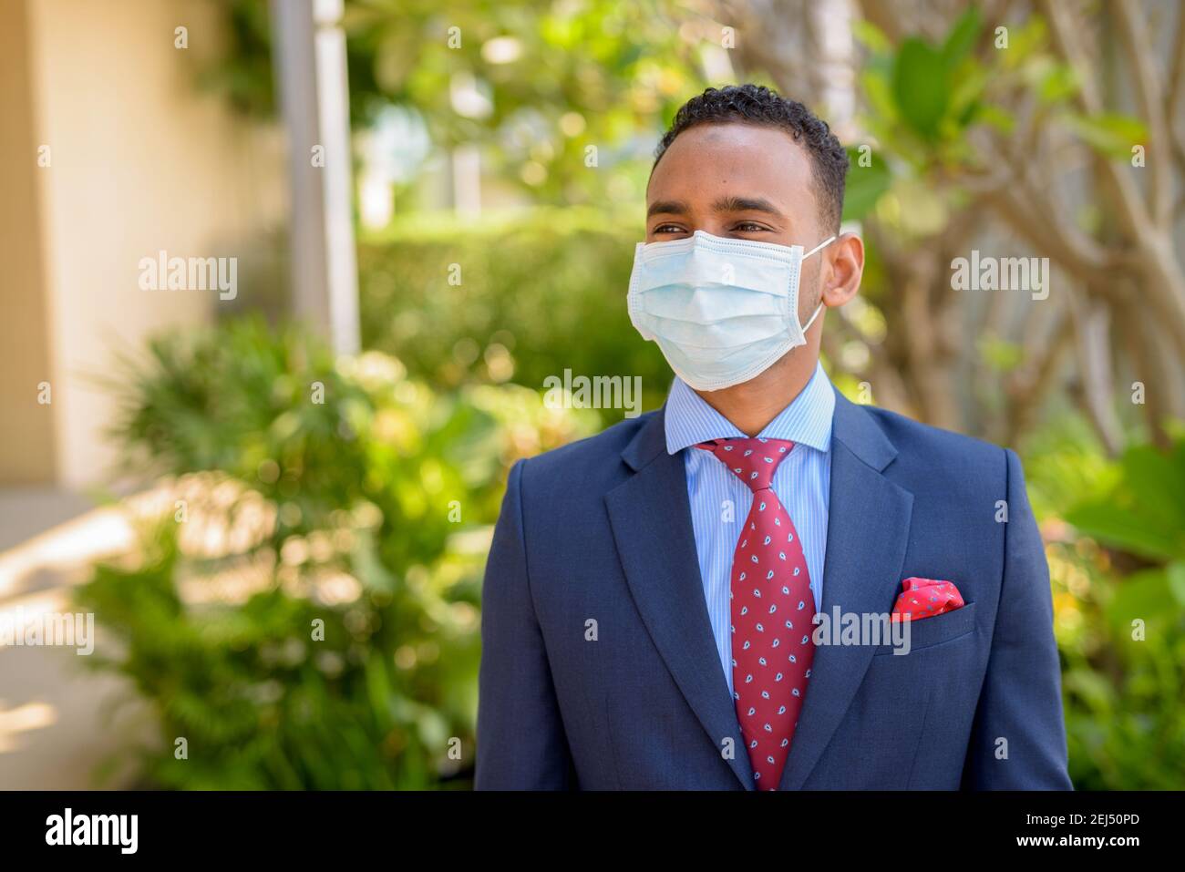 Uomo d'affari africano con maschera medica chirurgica per la protezione mentre si pensa all'aperto Foto Stock