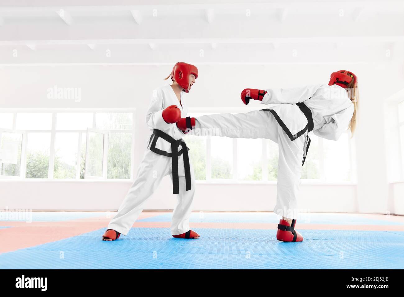 Due combattimenti professionali di karate femminile, utilizzando kick e punch tecnica karate in classe luminosa. Combattente in kimono bianco e glò rosso protettivo Foto Stock