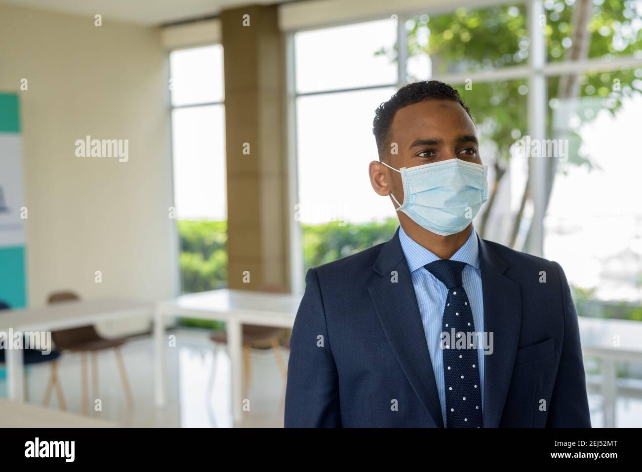 Uomo d'affari africano con maschera medica chirurgica per la protezione pensando a. ufficio Foto Stock