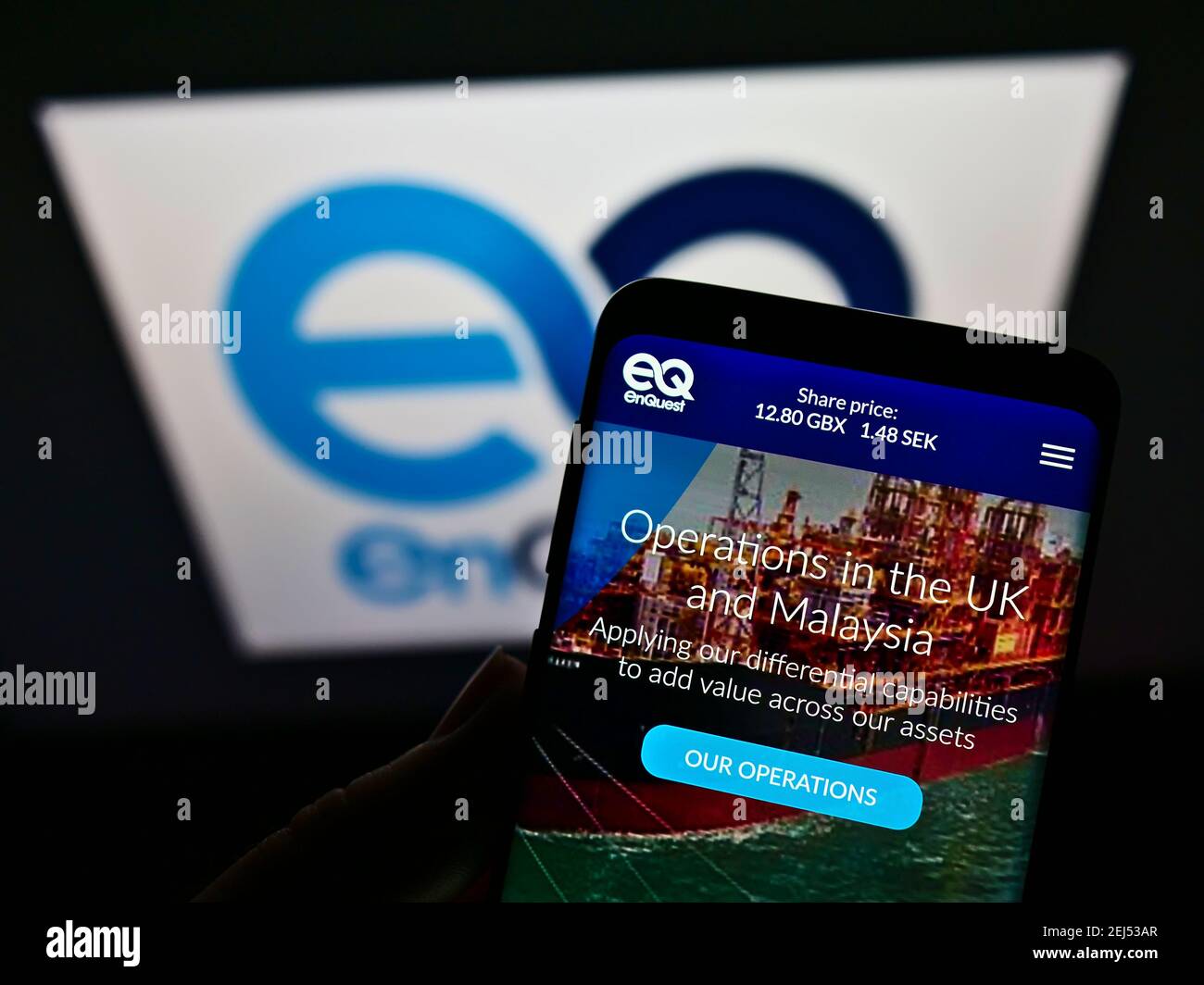 Persona che detiene il telefono cellulare con la pagina web della società britannica del petrolio e del gas EnQuest plc sullo schermo davanti al logo. Mettere a fuoco il centro del display del telefono. Foto Stock