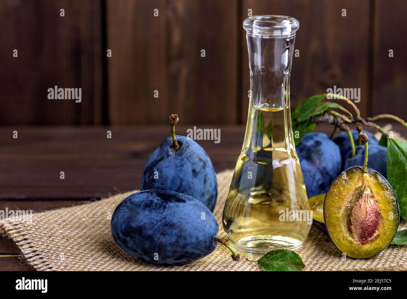 Brandy di prugne o schnapps in una piccola bottiglia di vetro con prugne fresche e gustose su un tavolo di legno. Messa a fuoco selettiva. Foto Stock