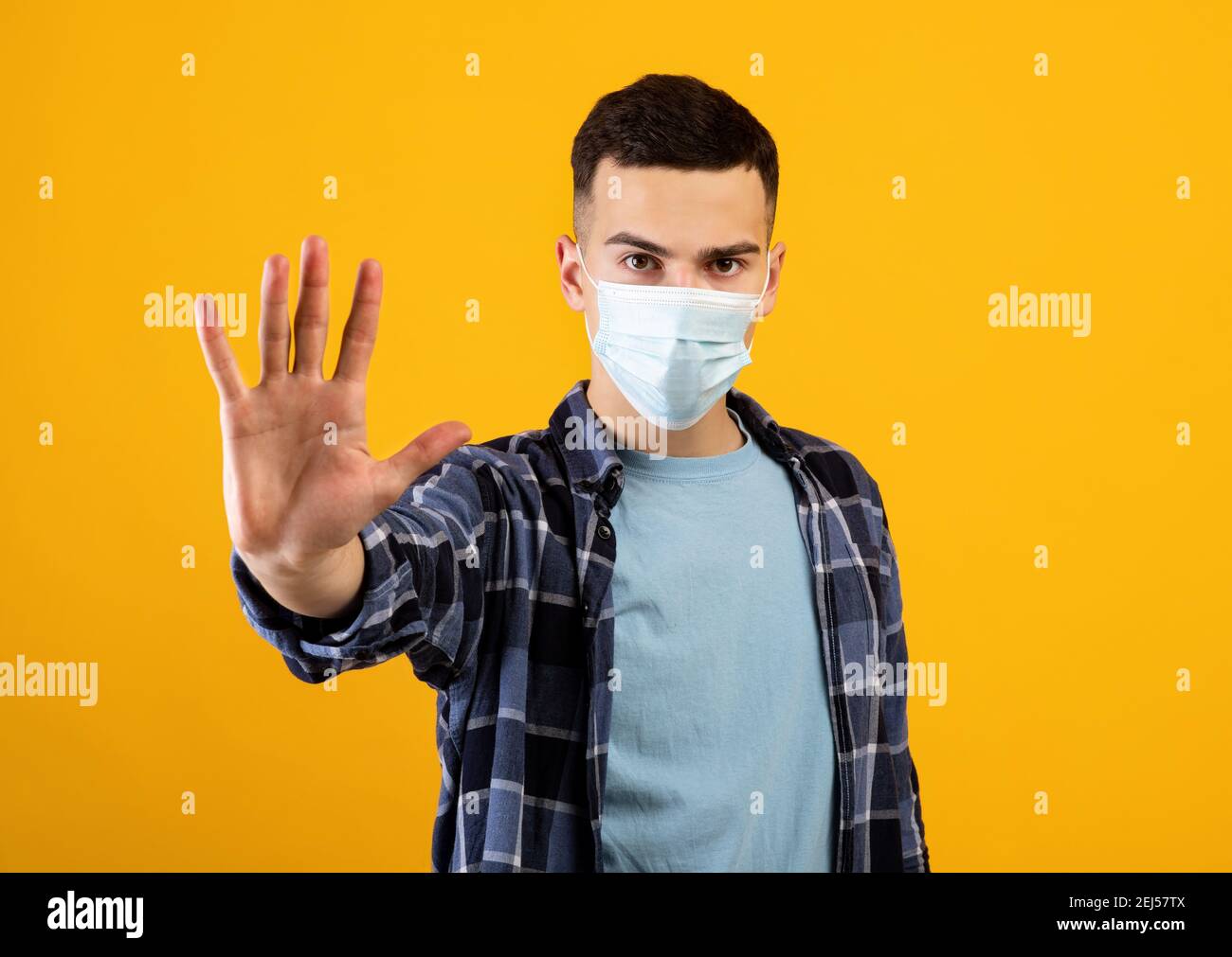Ragazzo millenario in maschera di faccia che gesturing STOP in studio arancione sfondo Foto Stock