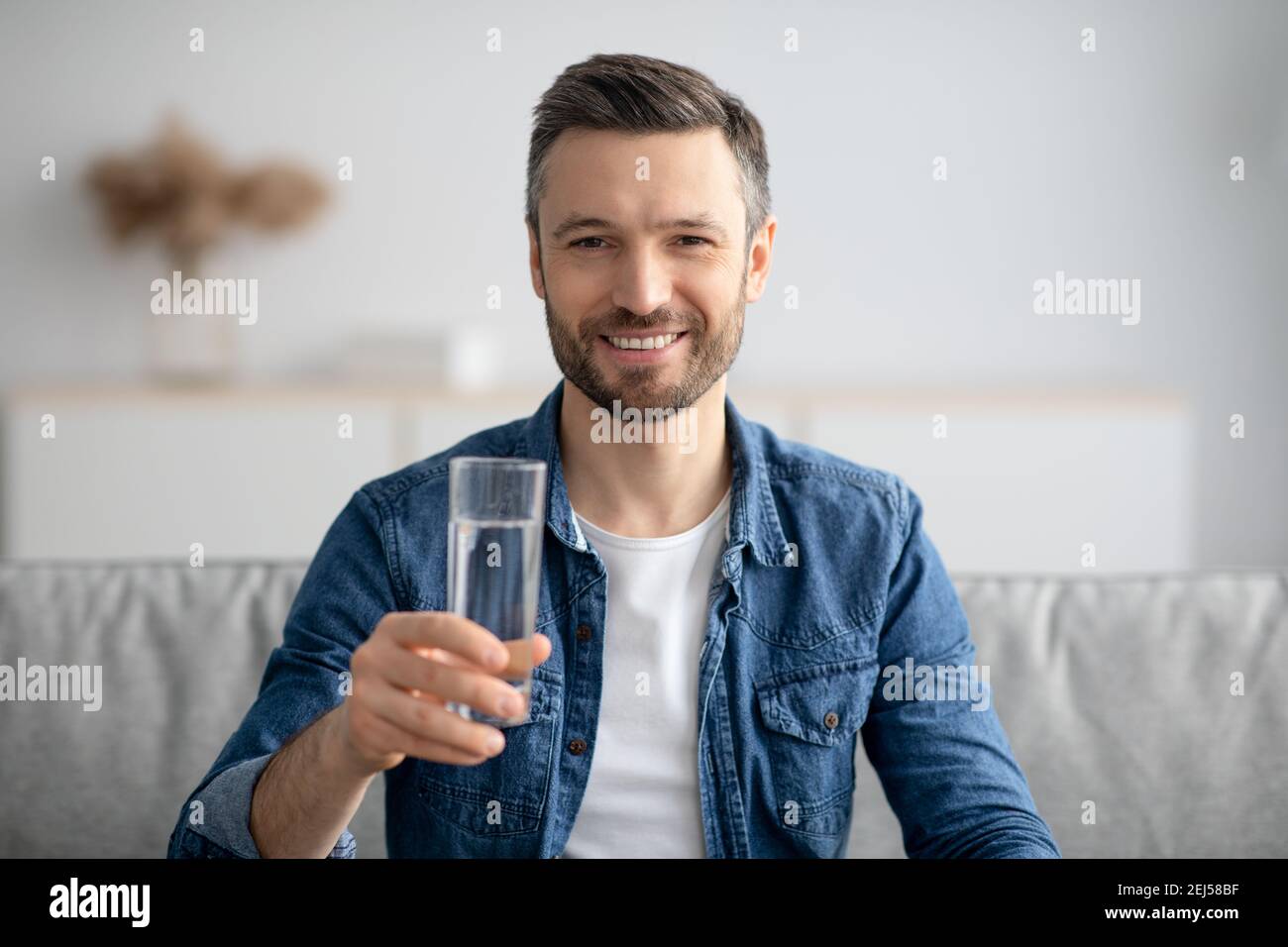 Uomo sano di mezza età che tiene un bicchiere d'acqua e sorridente Foto Stock