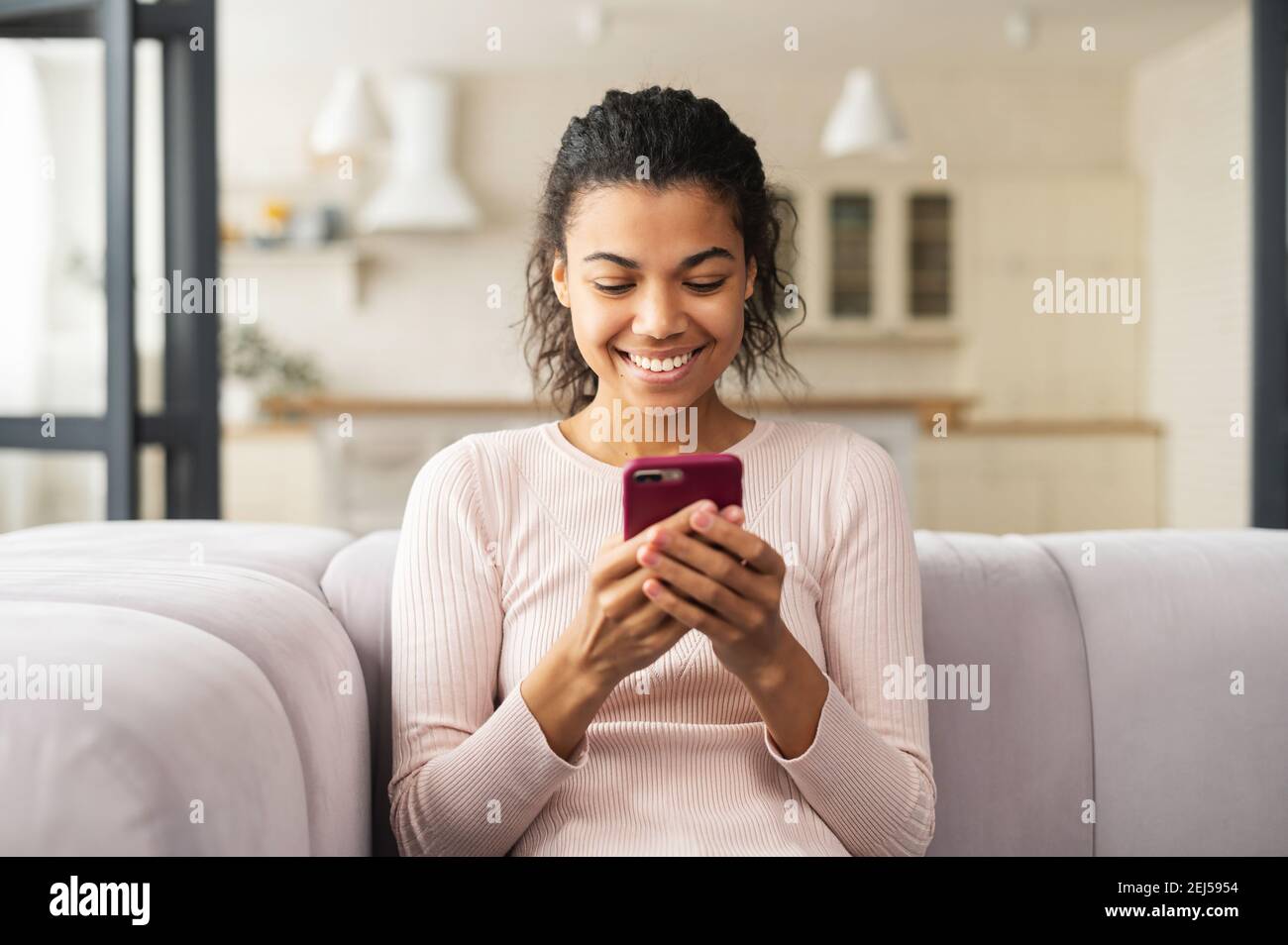 Giovane donna latina che chiacchiera al telefono e sorride molto, seduta su un comodo divano a casa, ha ricevuto un messaggio dalla famiglia, parlando via video, a lungo Foto Stock