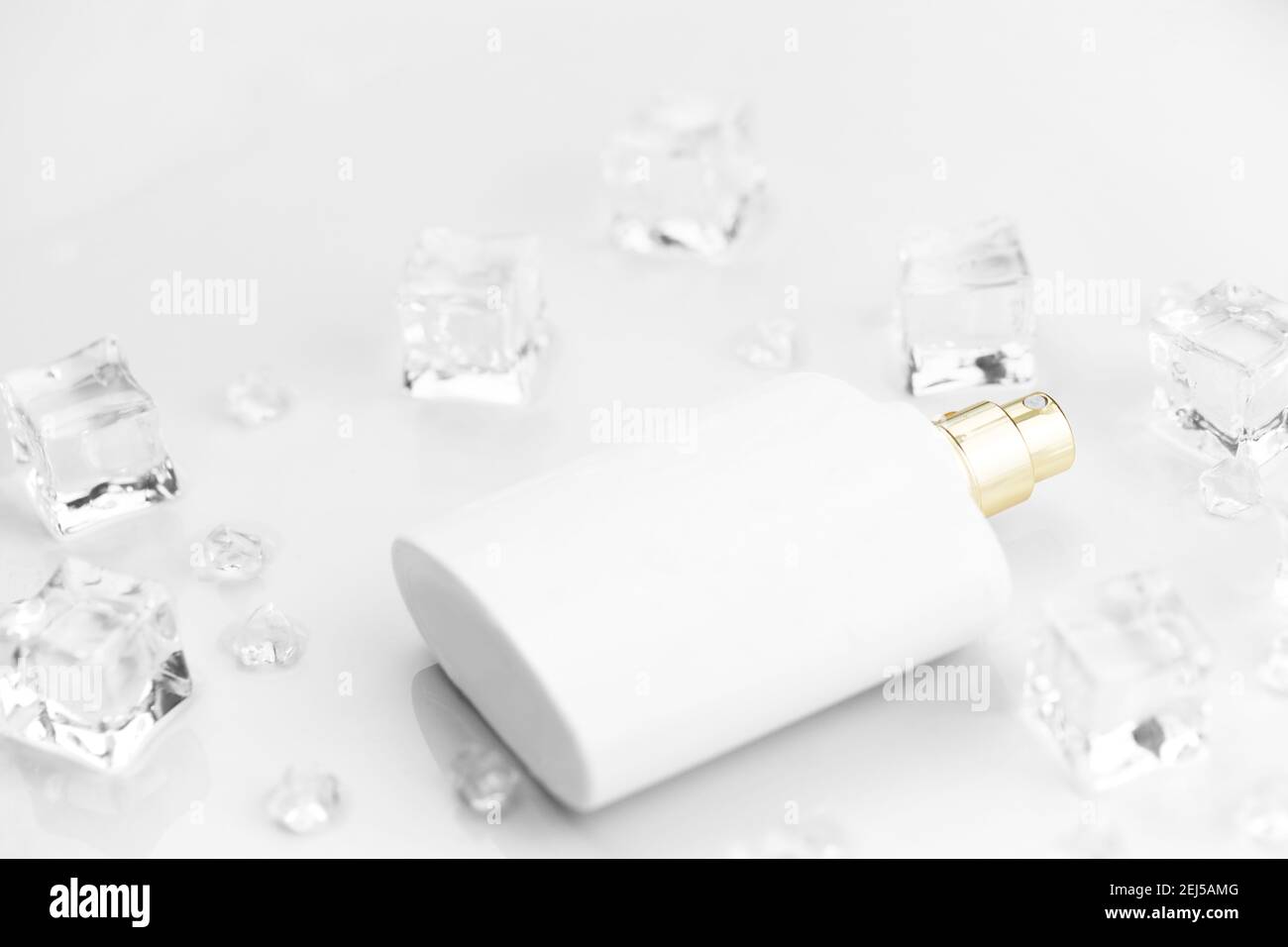 Bottiglia bianca di profumo femminile, fotografia obiettiva di bottiglia di profumo in cubetti di ghiaccio e acqua su tavola bianca. Vista dall'alto. Foto prodotto mockup, Foto Stock