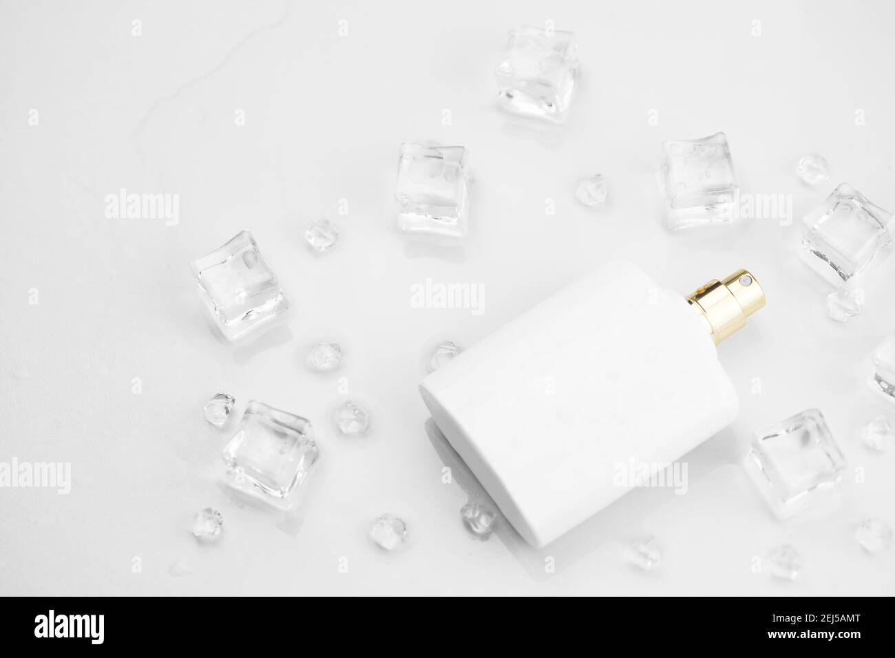 Bottiglia bianca di profumo femminile, fotografia obiettiva di bottiglia di profumo in cubetti di ghiaccio e acqua su tavola bianca. Vista dall'alto. Foto prodotto mockup, Foto Stock