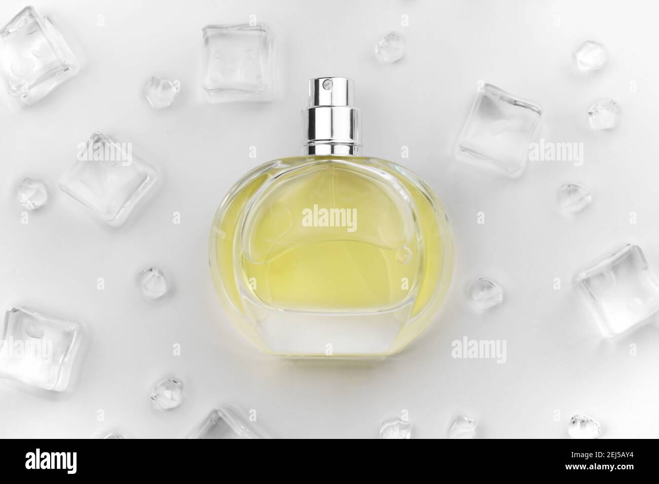 Bottiglia di profumo giallo femminile, Fotografia obiettivo di bottiglia di profumo in cubetti di ghiaccio e acqua su tavola bianca. Vista dall'alto. Foto prodotto mockup, con Foto Stock