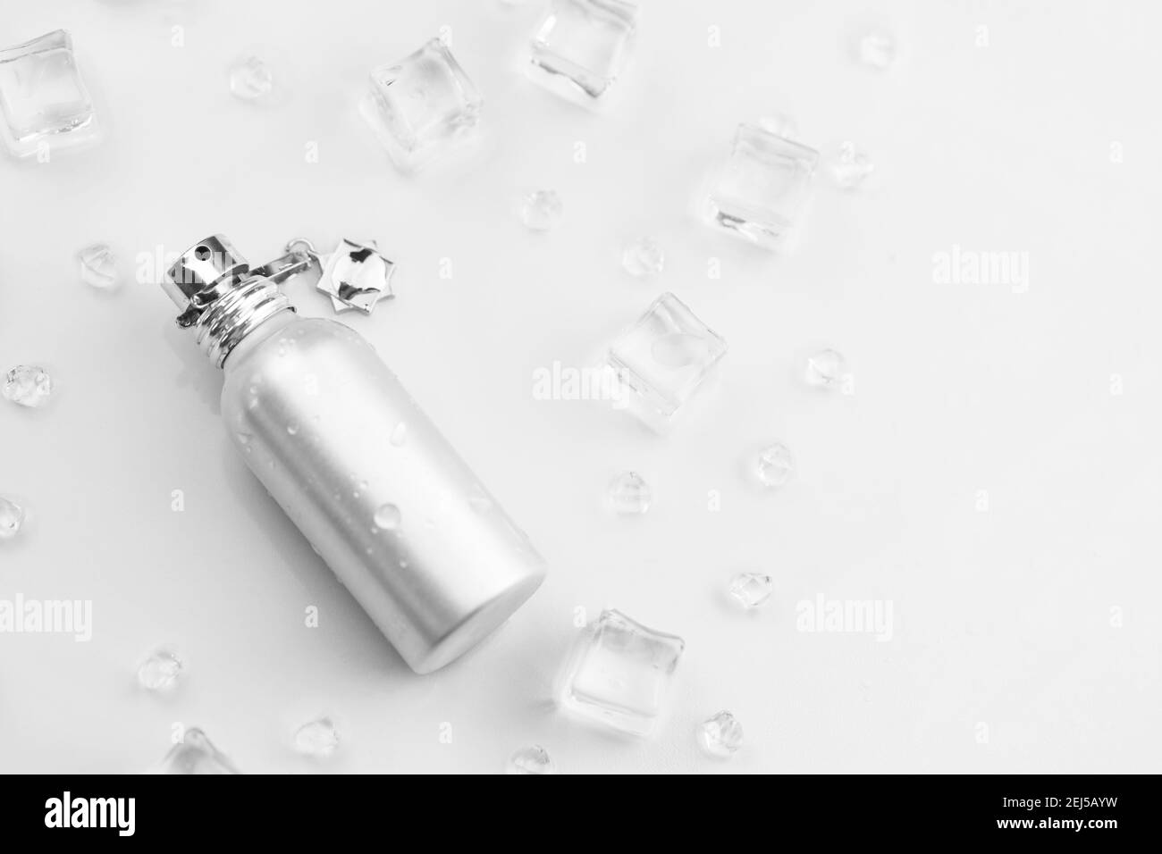 Bottiglia argentata di profumo femminile, Fotografia obiettivo di bottiglia di profumo metallico in cubetti di ghiaccio e acqua su tavola bianca. Vista dall'alto. Prodotto mockup Foto Stock