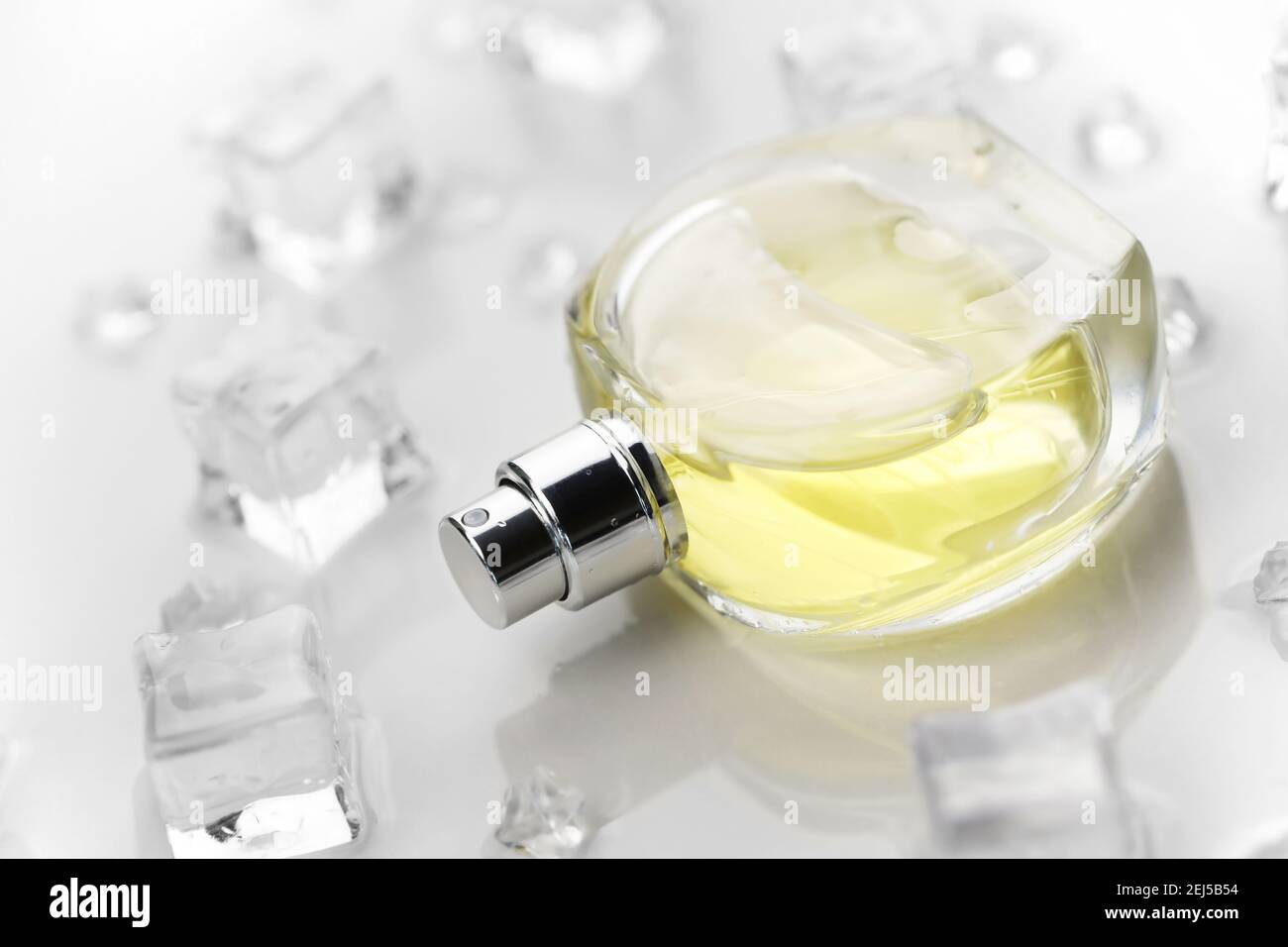 Bottiglia di profumo giallo femminile, Fotografia obiettivo di bottiglia di profumo in cubetti di ghiaccio e acqua su tavola bianca. Vista dall'alto. Foto prodotto mockup, con Foto Stock
