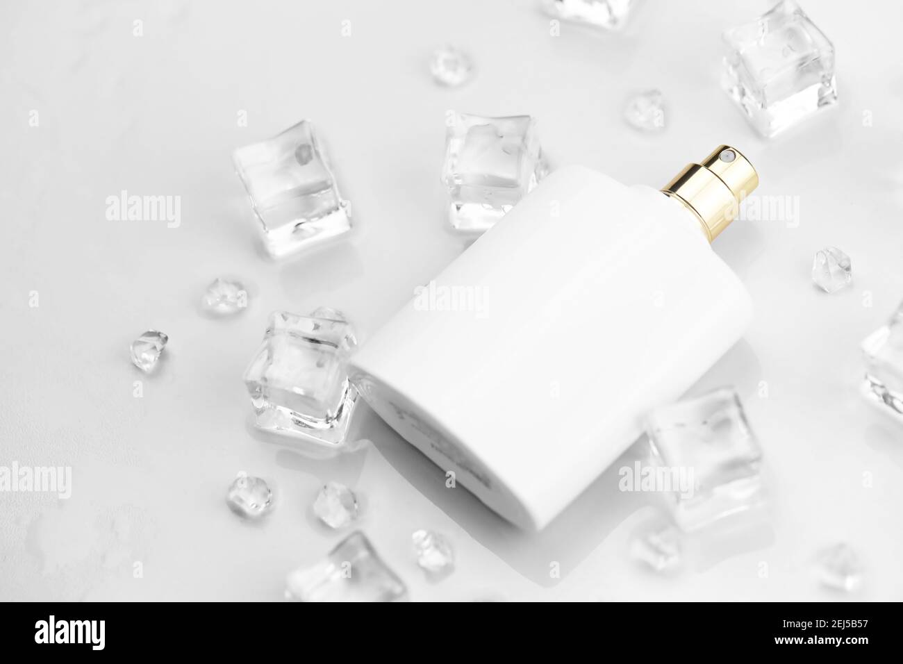 Bottiglia bianca di profumo femminile, fotografia obiettiva di bottiglia di profumo in cubetti di ghiaccio e acqua su tavola bianca. Vista dall'alto. Foto prodotto mockup, Foto Stock