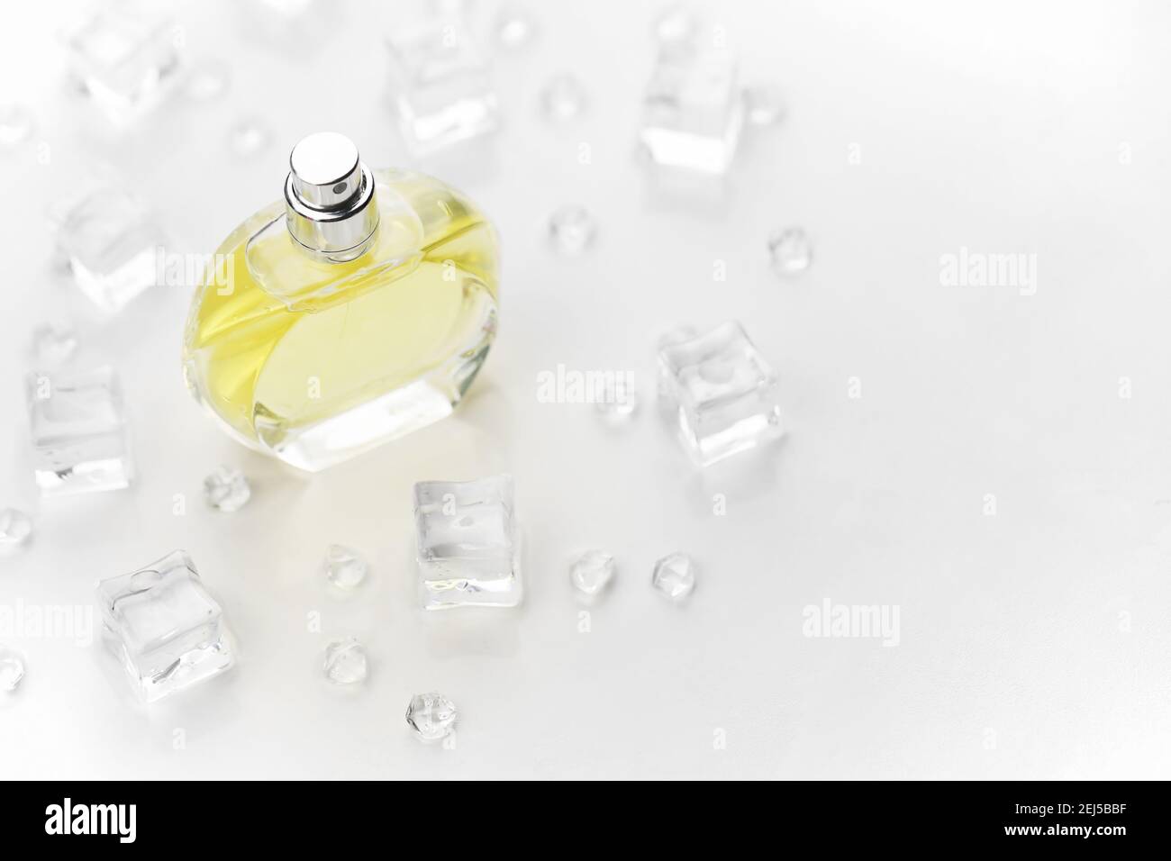 Bottiglia di profumo giallo femminile, Fotografia obiettivo di bottiglia di profumo in cubetti di ghiaccio e acqua su tavola bianca. Vista dall'alto. Foto prodotto mockup, con Foto Stock