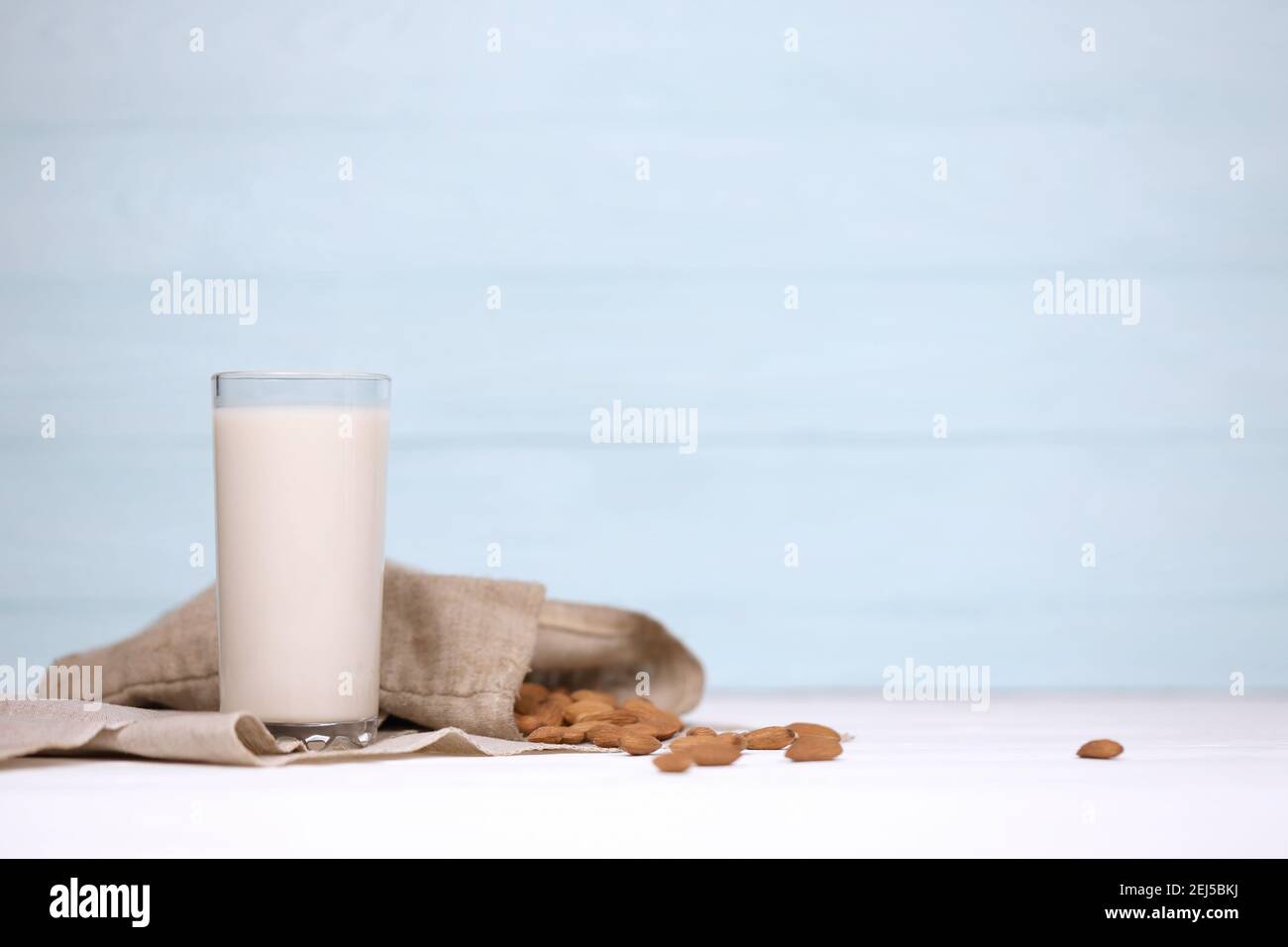 Bicchiere di latte di mandorle con noci di mandorle su tela su tavola di legno bianco. Latte latte alternativo per disintossicazione, alimentazione sana e diete. Selettivo fo Foto Stock
