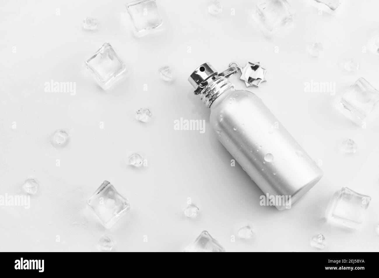 Bottiglia argentata di profumo femminile, Fotografia obiettivo di bottiglia di profumo metallico in cubetti di ghiaccio e acqua su tavola bianca. Vista dall'alto. Prodotto mockup Foto Stock