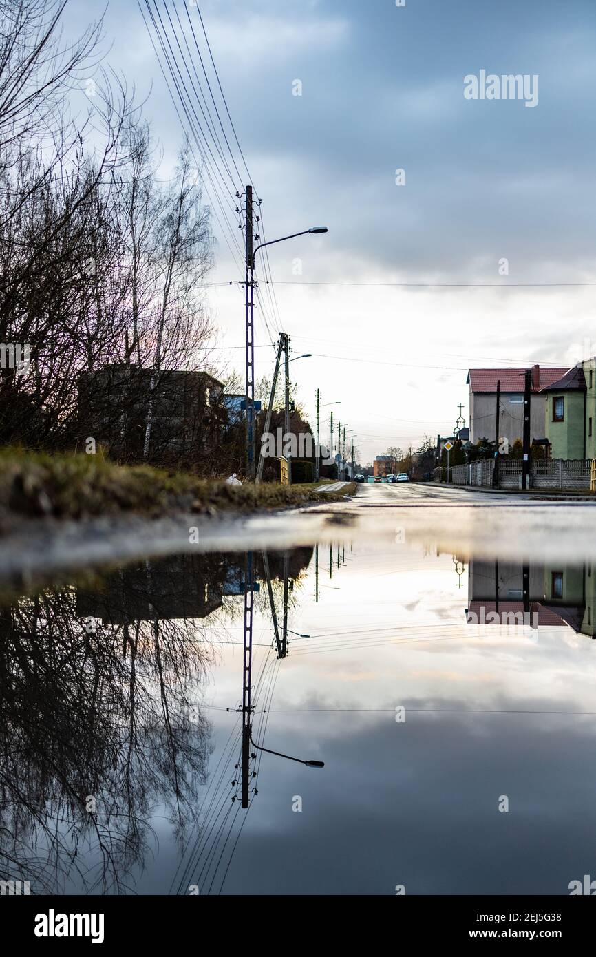 Zawiercie, Polonia - Febbraio 18 2020 lungo strada riflessa in puddle al tramonto nuvoloso Foto Stock