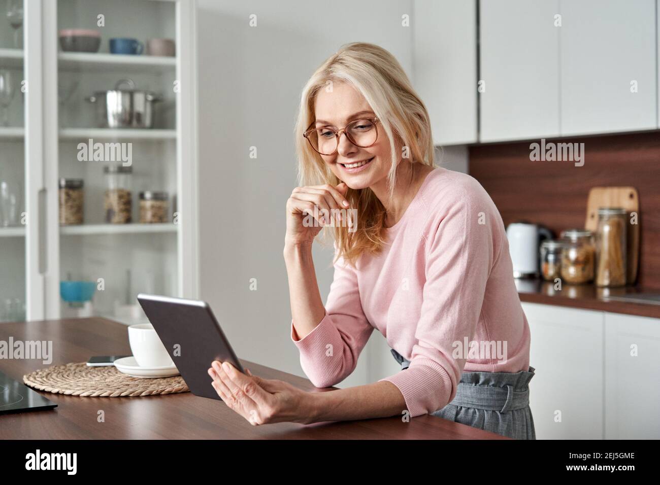 Donna felice di mezza età di 50 anni che usa la tavoletta a casa. Foto Stock