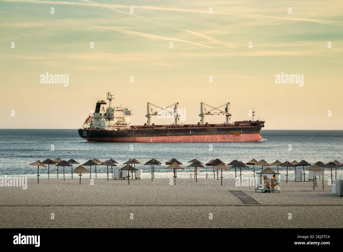 Setúbal, Portogallo - 29 agosto 2020: Nave da carico che passa dalla spiaggia di Figueirinha a Setúbal, Portogallo, al tramonto, con gli ombrelloni e la sabbia nel f Foto Stock