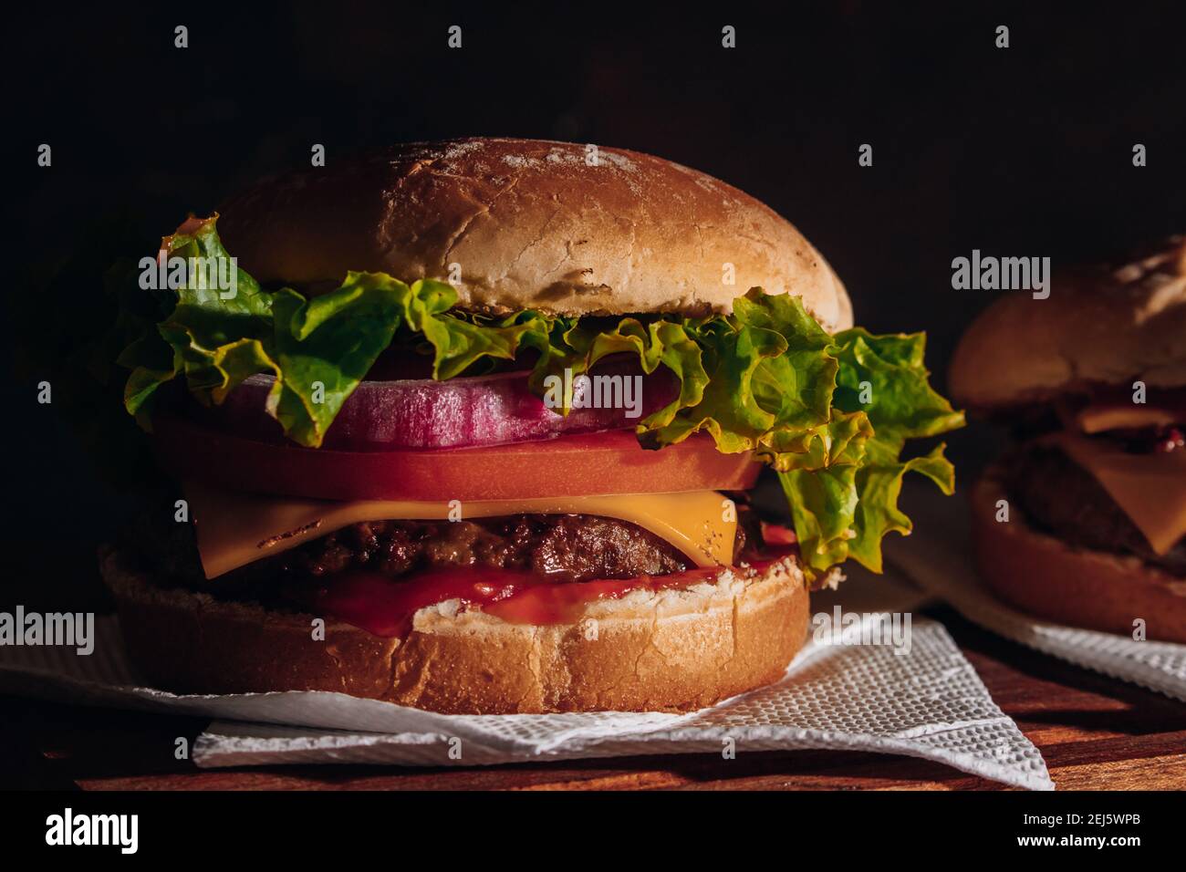 Deliziosi hamburger con lattuga, pomodoro e cipolla rossa e pancetta su pane fatto in casa con semi e ketchup su una superficie di legno. Foto Stock