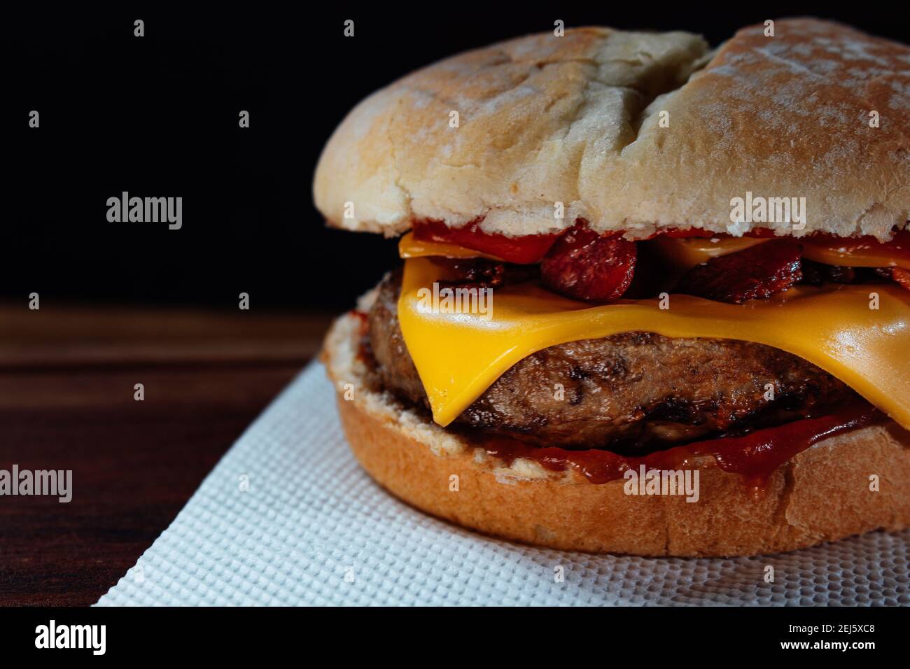 Hamburger delizioso con pancetta e formaggio cheddar su pane fatto in casa con semi e ketchup su una superficie di legno. Foto Stock