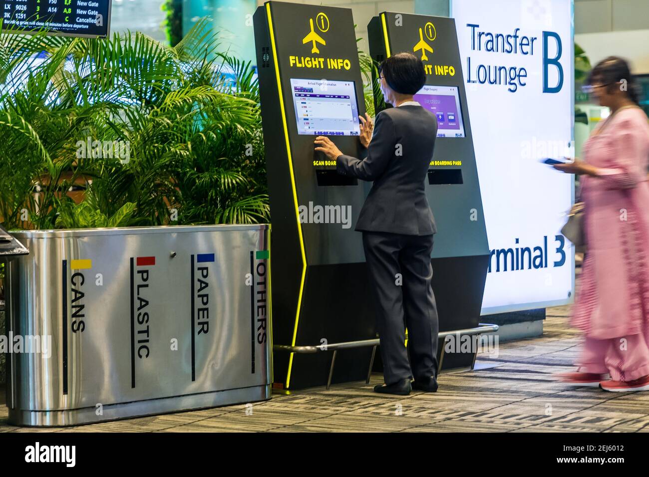 Una donna sta usando un'interfaccia di informazioni dell'aeroporto, mentre un'altra donna è waiting.on il lato sinistro tre bidoni della spazzatura. Foto Stock