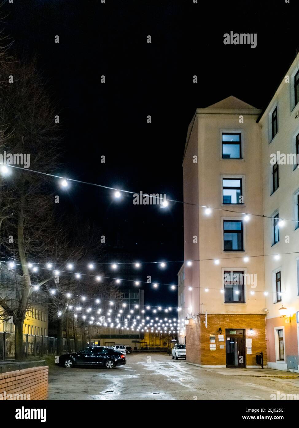 Lodz, Polonia - Febbraio 21 2020 piccola piazza vicino alla vecchia casa con luci appese incandescenti Foto Stock