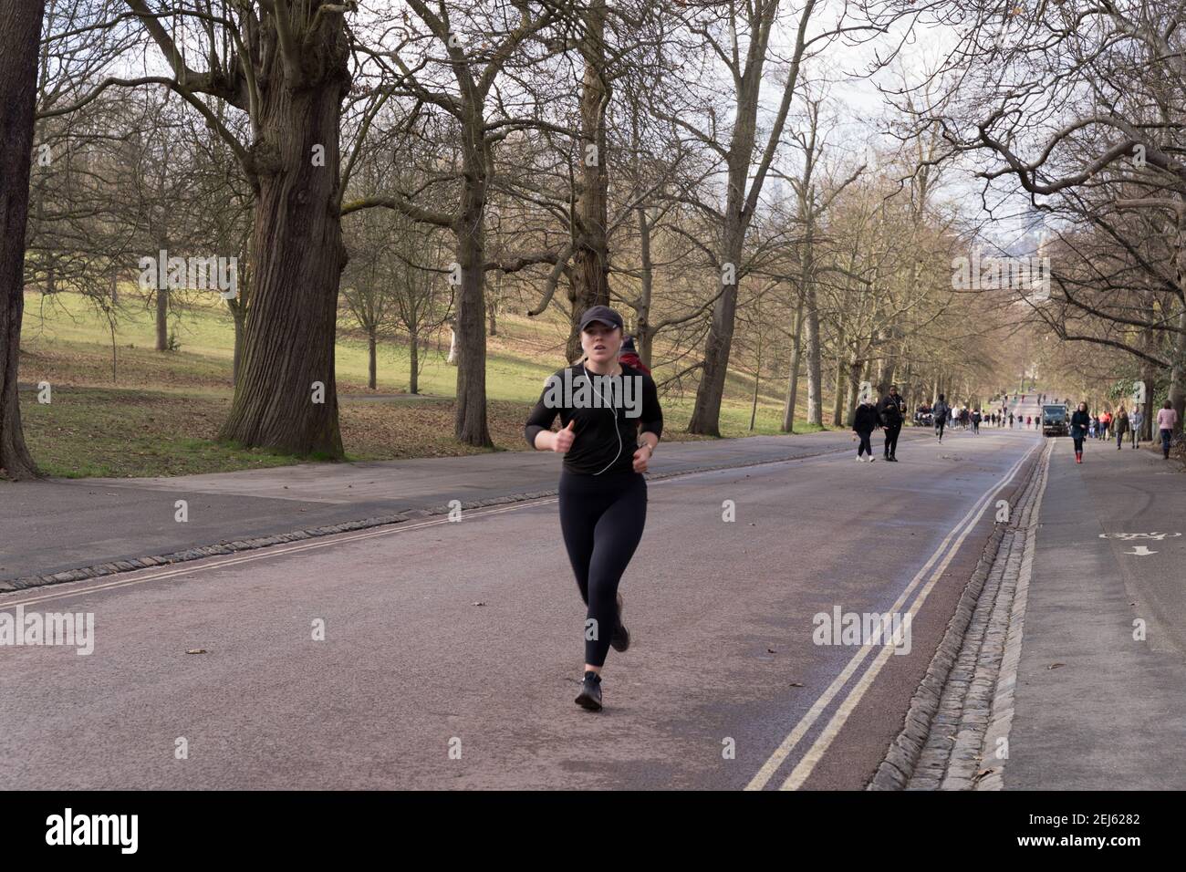 Una donna runner in tuta nera con cappuccio base a sfera Correre in salita mentre si ascolta la musica con le cuffie a Londra Greenwich Park Foto Stock