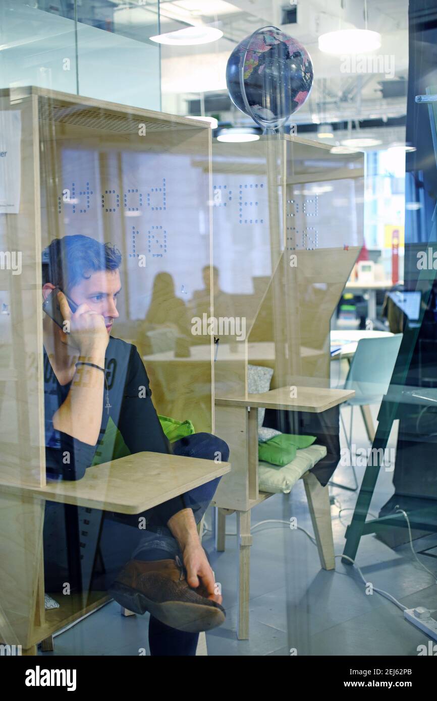 Uomo d'affari alla scrivania in un armadio in un moderno spazio di lavoro per ufficio Utilizzo del telefono cellulare Foto Stock