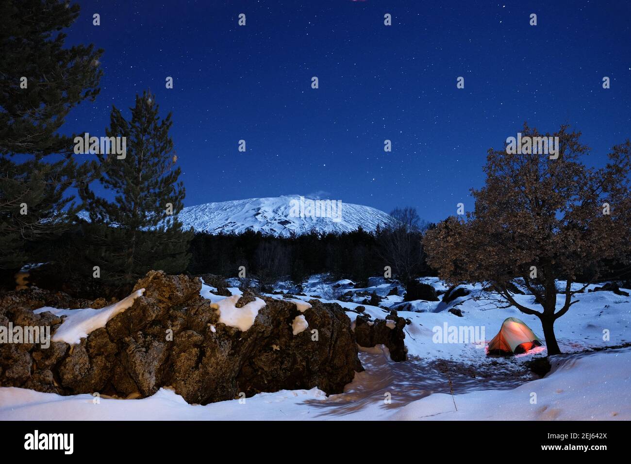 Formazione rocciosa 'ciara' e tenda luminosa nella neve del Parco dell'Etna sotto il cielo stellato, Sicilia Foto Stock