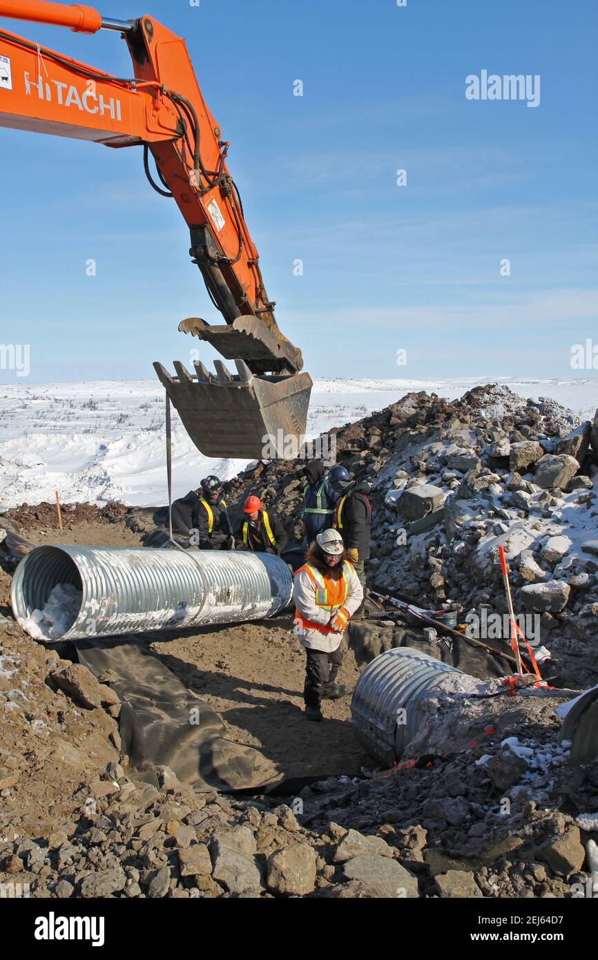 Hitachi Excavator e lavoratori che installano culvert durante la costruzione invernale dell'autostrada Inuvik-Tuktoyaktuk, territori del Nord-Ovest, Artico del Canada. Foto Stock