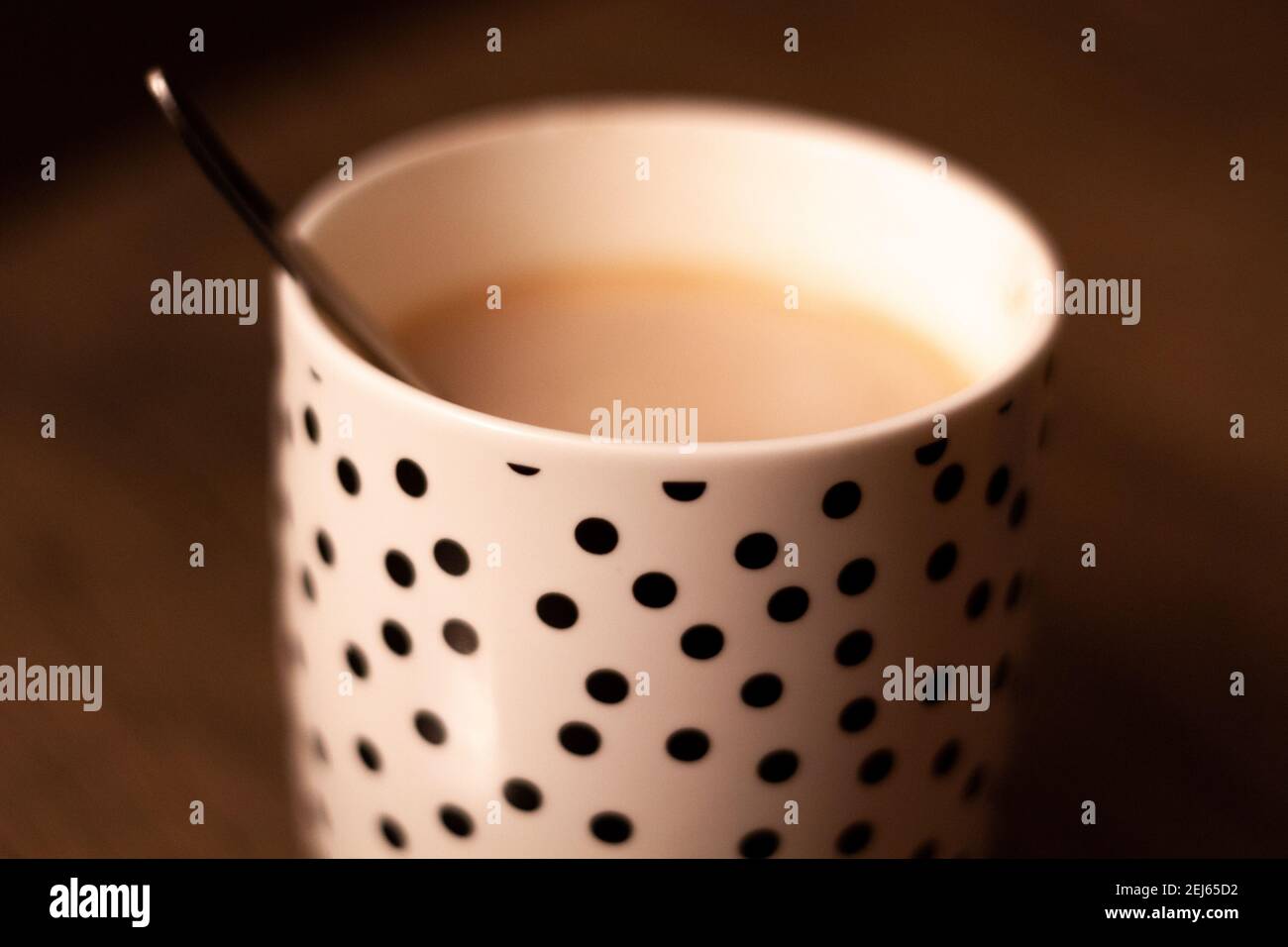 Primo piano di una tazza bianca con punti neri con a. bevanda calda e un cucchiaio di metallo su un tavolo di legno Foto Stock
