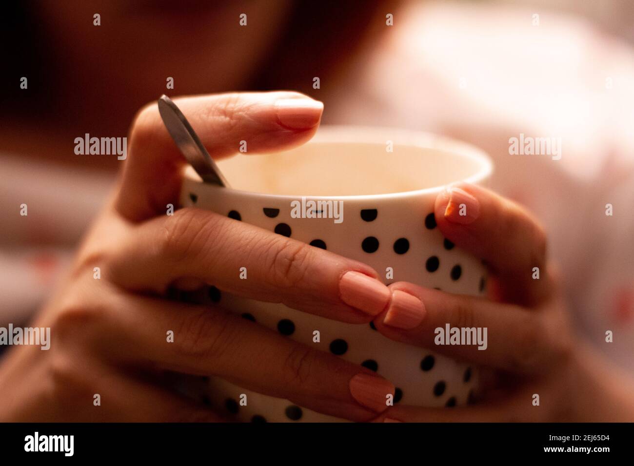 Dettaglio delle mani di una donna che tiene un bianco tazza in porcellana con puntini neri contenente una bevanda calda Foto Stock