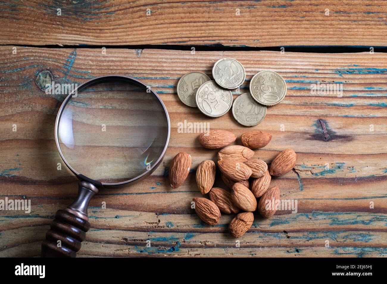 Lente di ingrandimento, centesimi di euro e noci su un tavolo di legno. Foto Stock