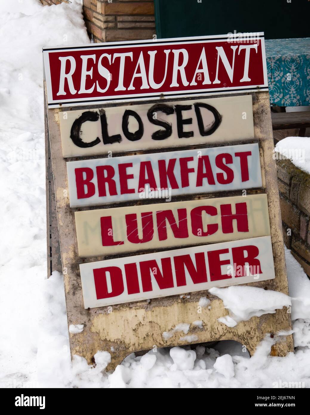 Un vecchio cartello coperto di neve davanti ad un ristorante chiuso, un segno dell'economia depressa a causa della pandemia COVID-19. Foto Stock