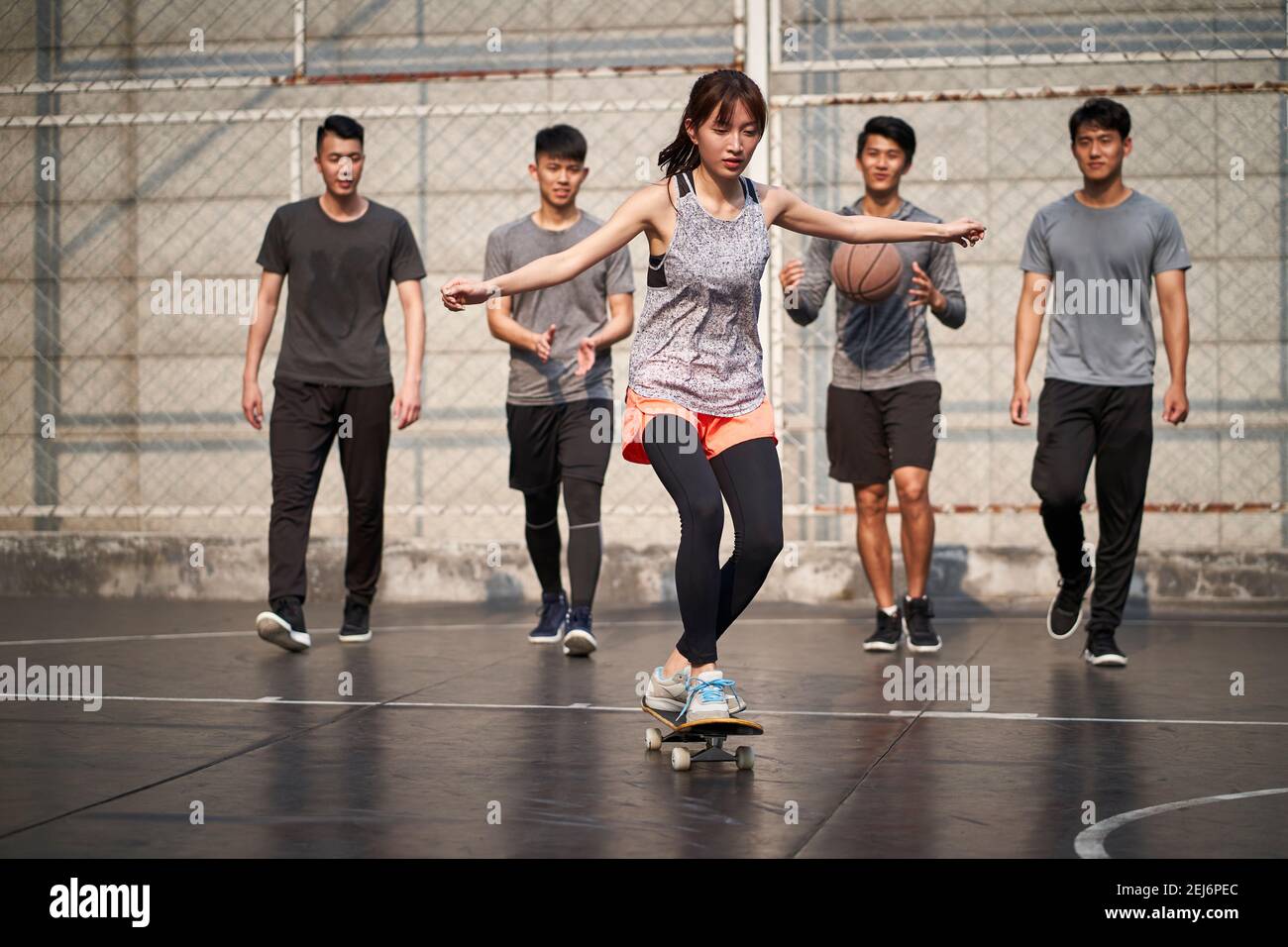 giovane donna asiatica skateboarder skateboarder all'aperto con amici che guardano da dietro Foto Stock