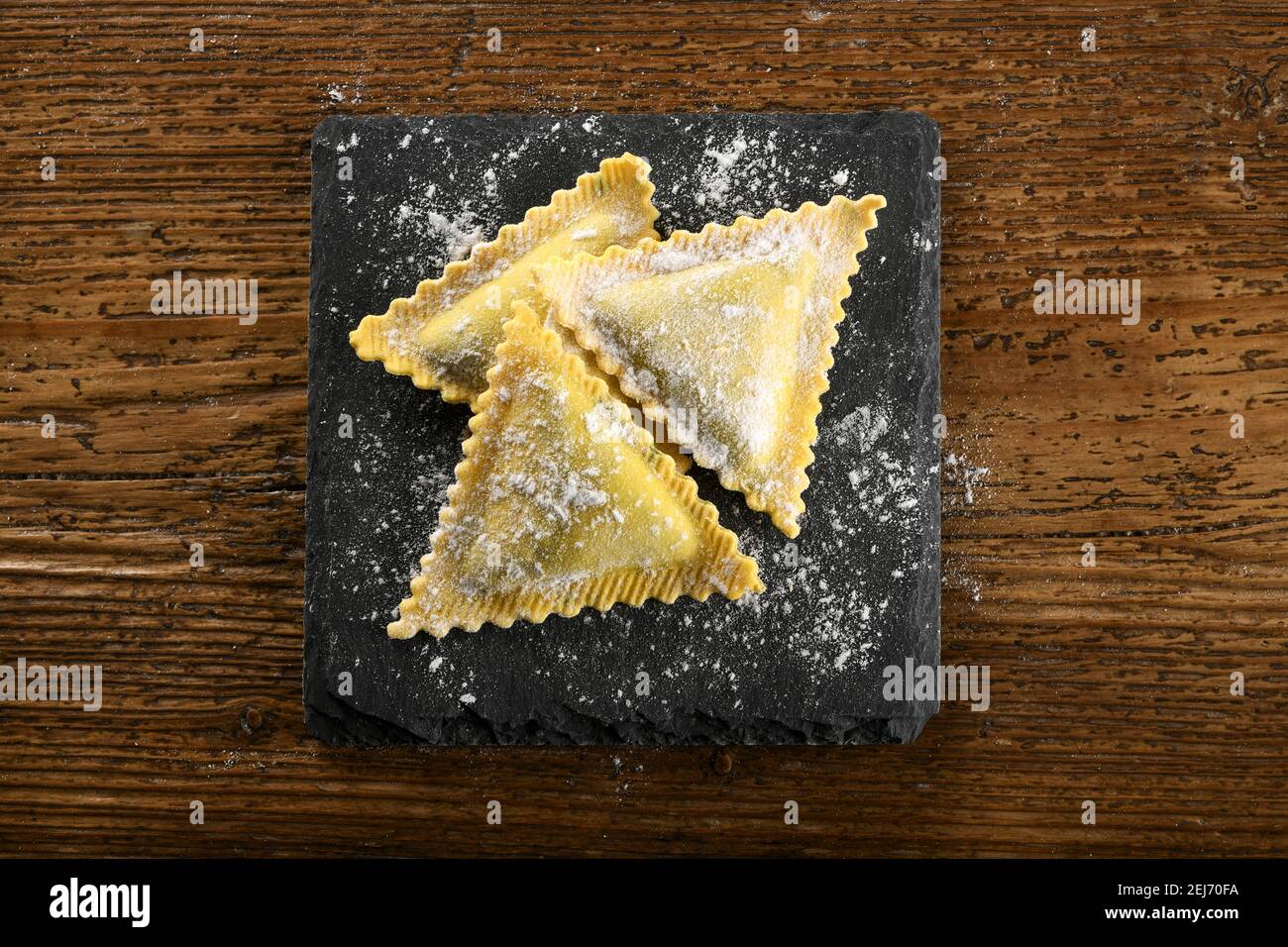 Ravioli freschi e triangolari ripieni crudi pasta italiana su A. tavola sgocciolata con farina vista in alto su un legno tabella Foto Stock